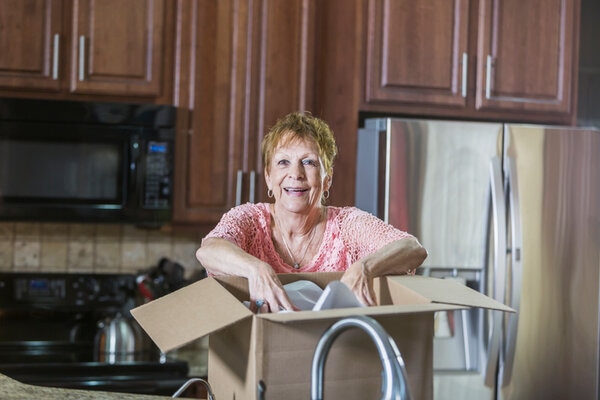 Senior Woman Moving House In Kitchen With Cardboard Box Senior Woman Moving House In Kitchen With Cardboard Box