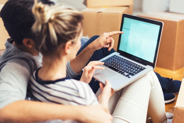 Young Couple Sitting Between Boxes And Using A Laptop Young Couple Sitting Between Boxes And Using A Laptop
